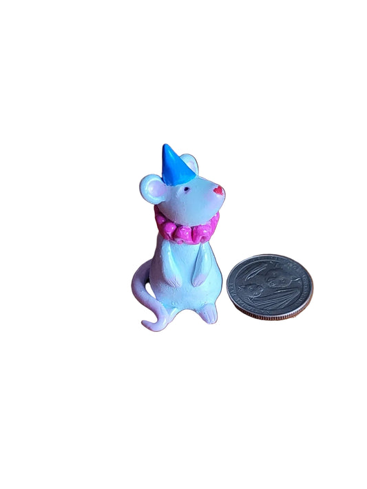 Small figurine of a mouse with a blue hat and pink collar next to a coin on a wooden surface